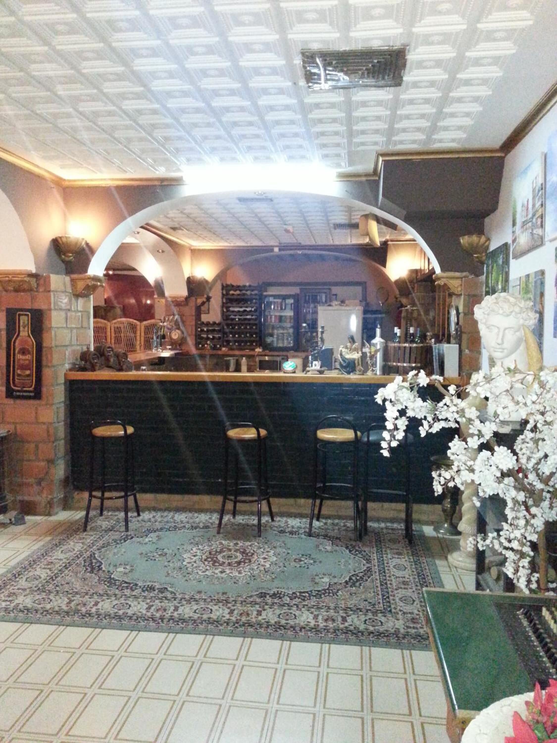 Un espace bar comprenant un comptoir, trois tabourets, un tapis à motifs et une plante décorative.