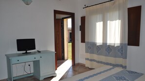 Ein Schlafzimmer mit einem Bett, einem Schreibtisch mit Fernseher und einem Fenster mit Vorhängen.