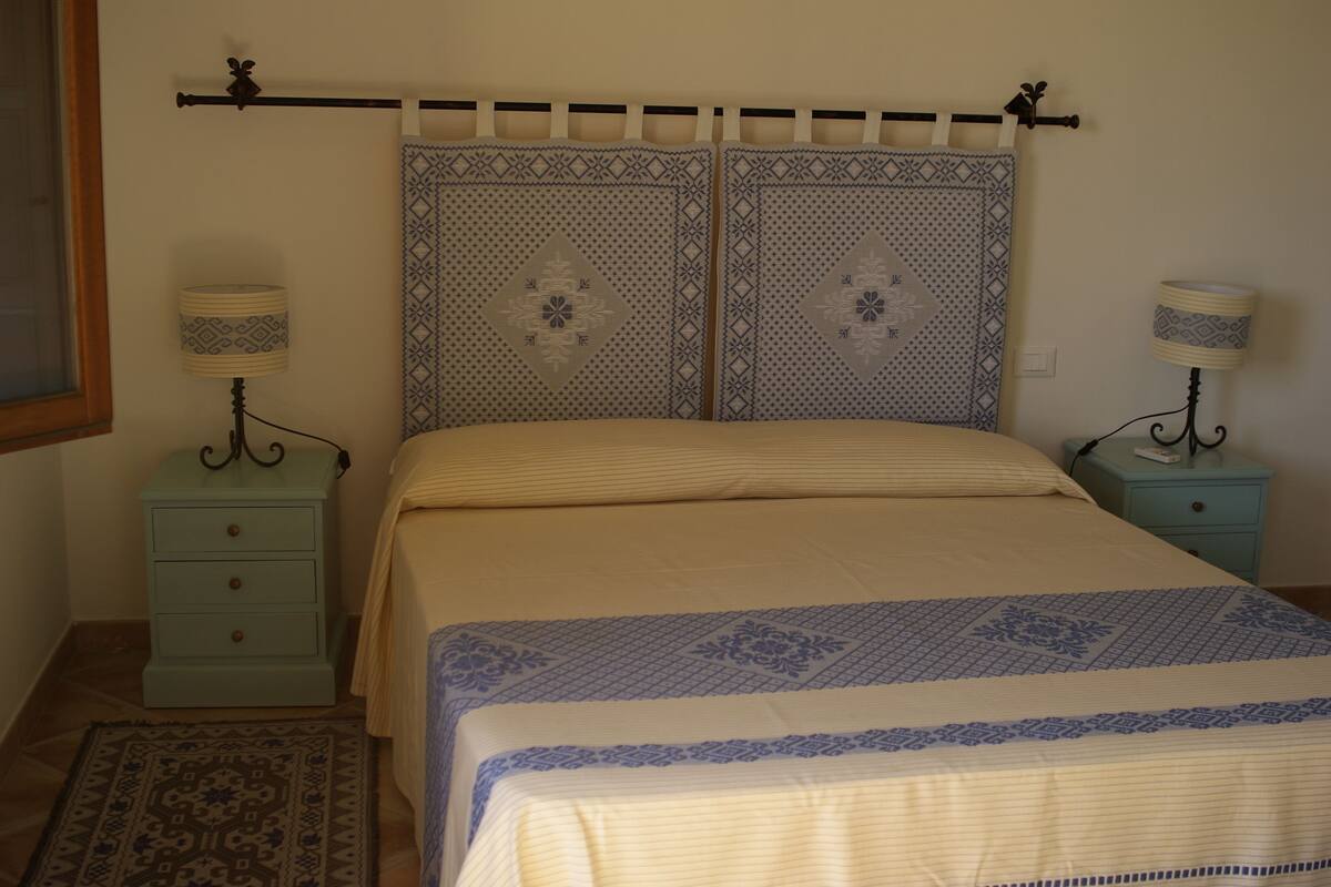 Ein Schlafzimmer mit einem Bett, zwei Nachttischen, einem gemusterten Kopfteil und einem dekorativen Wandbild.