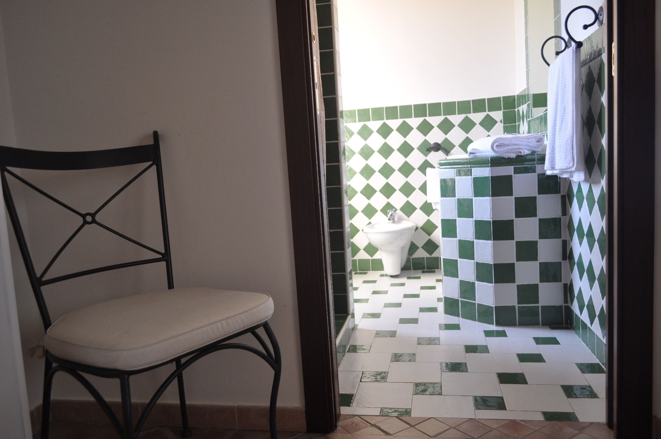 Un baño con piso a cuadros, un inodoro y una silla.