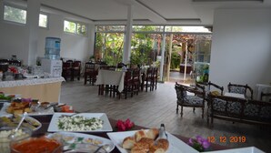 Un grand espace dédié à la salle à manger, avec plusieurs tables et chaises, un distributeur d’eau et une vue sur l’extérieur.