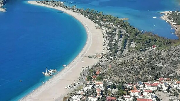 Une vue aérienne d’une zone côtière avec une plage en forme de courbe, des bateaux et des bâtiments.