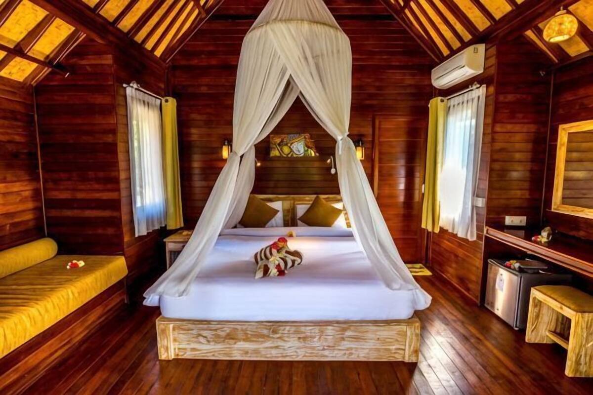 Ein Zimmer in einer Holzhütte mit einem Baldachinbett, einem kleinen Tisch und einer Bank.