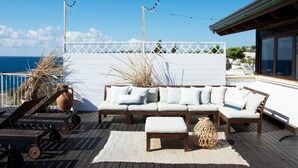 Eine sonnendurchflutete Terrasse im Freien mit einer Holzliege, Lounge-Stühlen und einem dekorativen Teppich.