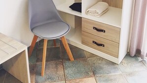 Ein kleines Zimmer mit Schreibtisch, Stuhl, Kleiderschrank und Bett.