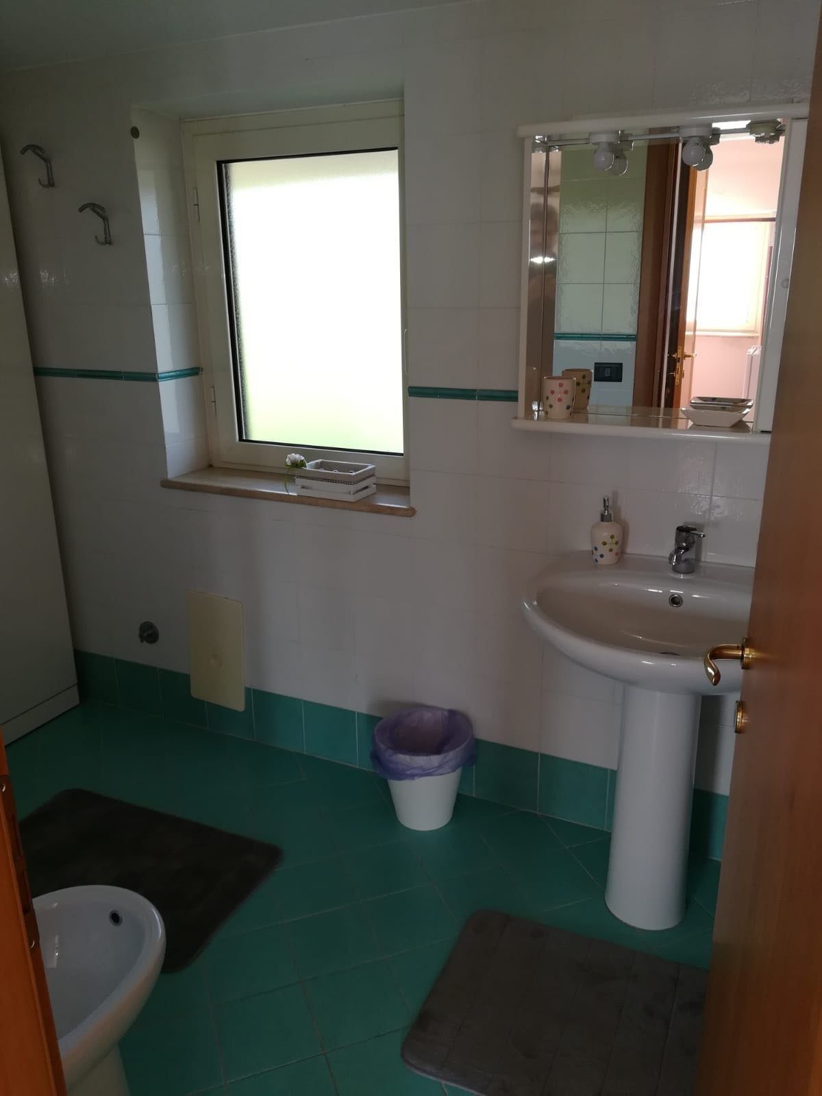 A bathroom with a window, a sink, a bidet, and a toilet.