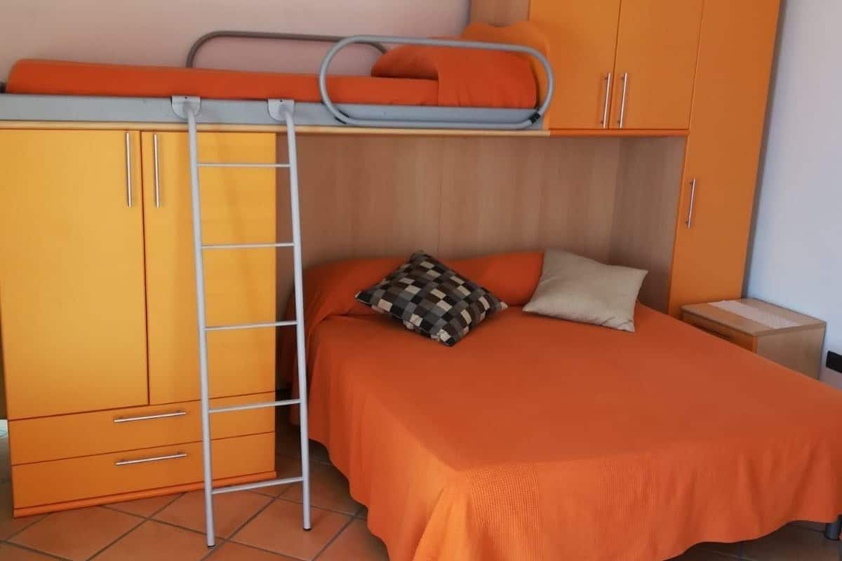 A dormitory room with a bunk bed, a wardrobe, and a bedside table.
