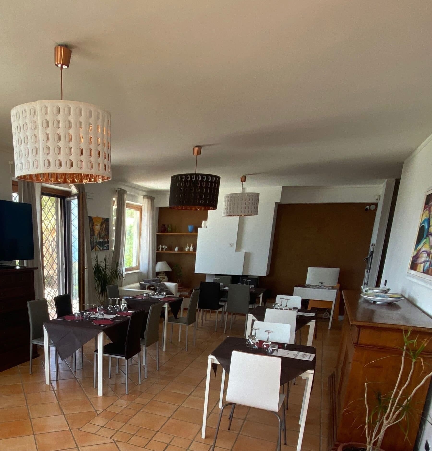 Un comedor con varias mesas y sillas, un televisor y un amplio ventanal con cortinas.