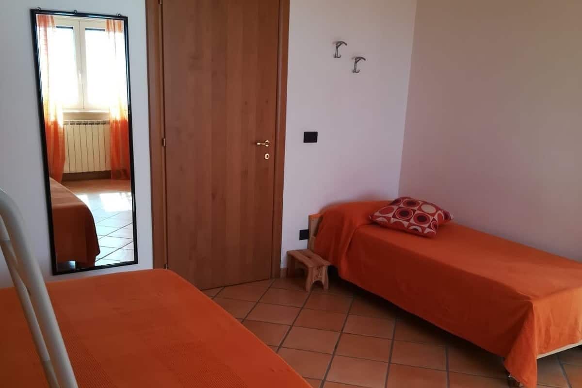 A room with two beds, a wooden door, a small stool, and a mirror on the wall.