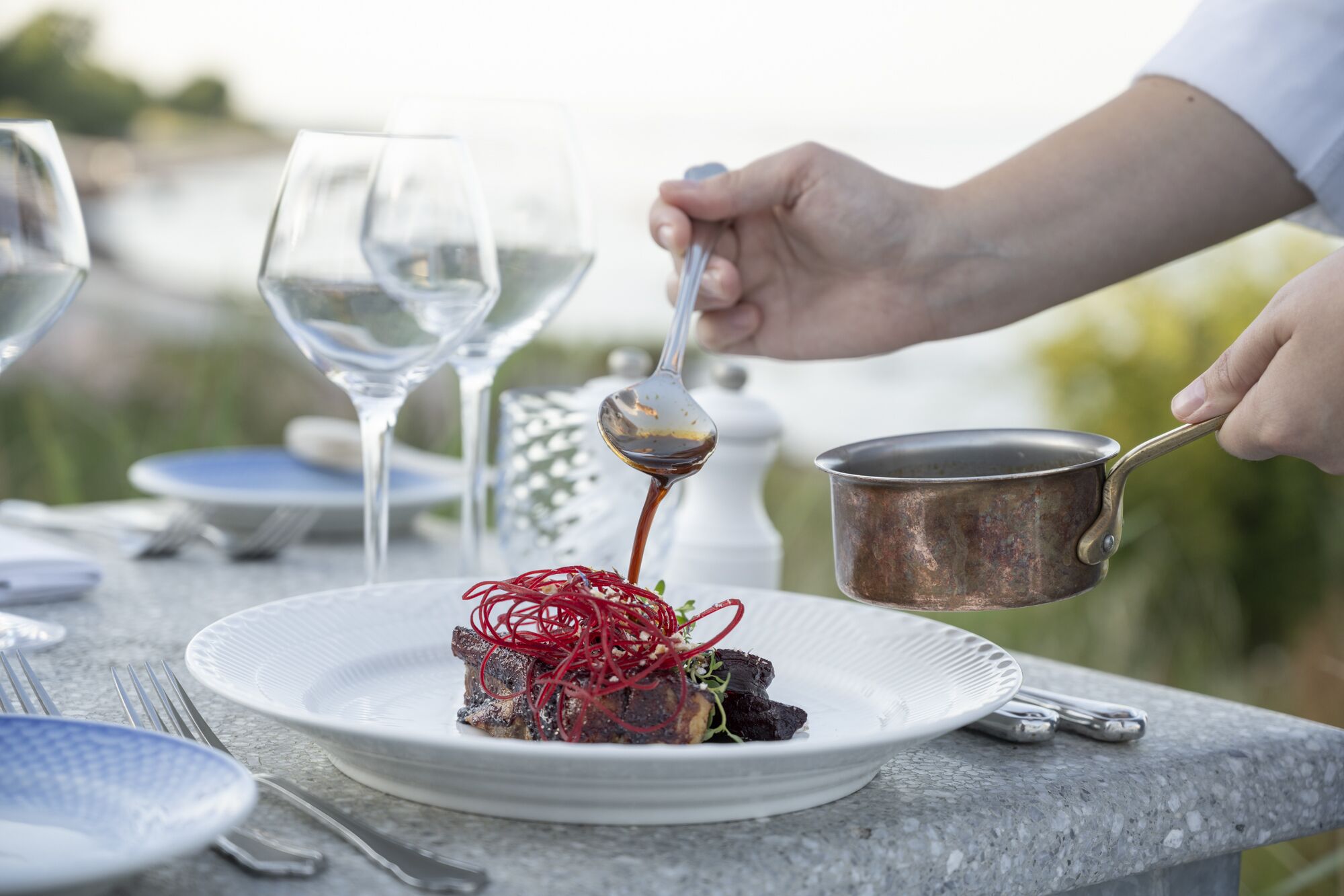 A dining table with a plate of food, a spoon, and a pot.
