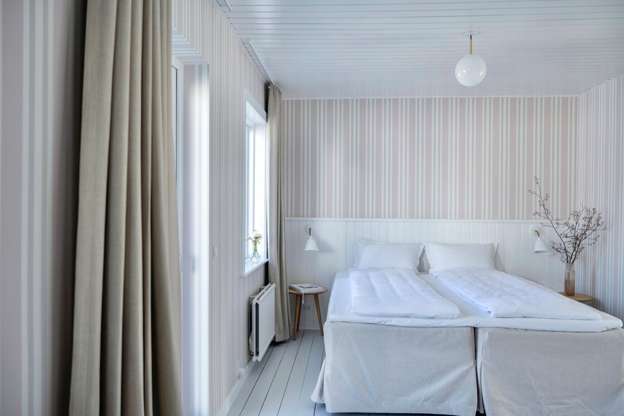 Ein Hotelzimmer mit einem großen Bett, einem kleinen Nachttisch, einem Heizkörper und einem Fenster mit Vorhängen.