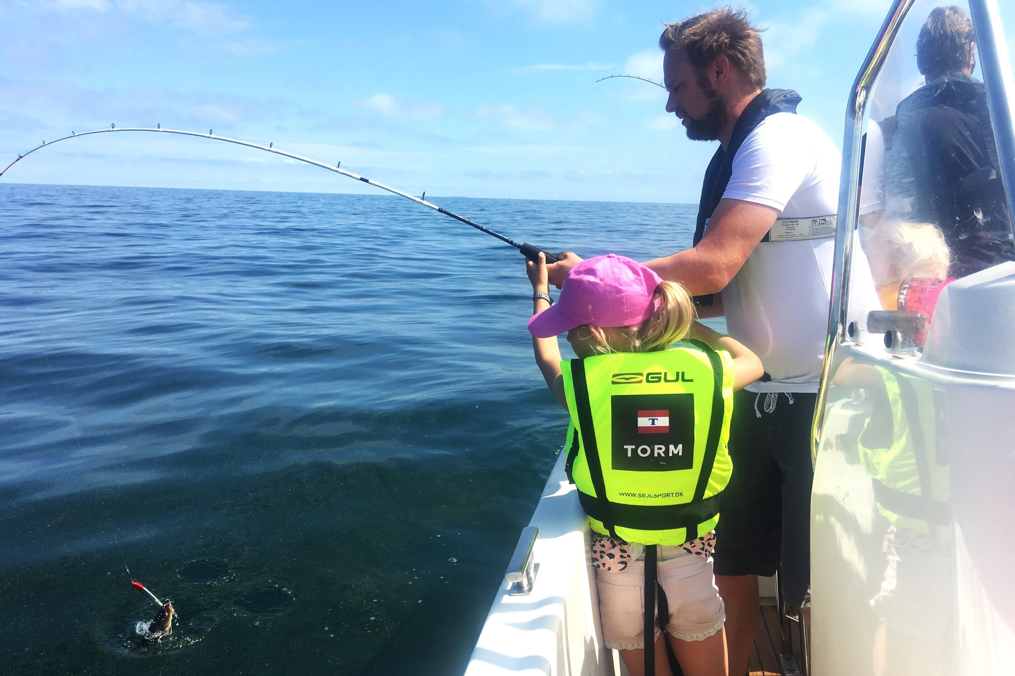 A boat with two people fishing, one wearing a life jacket labeled "TORM".