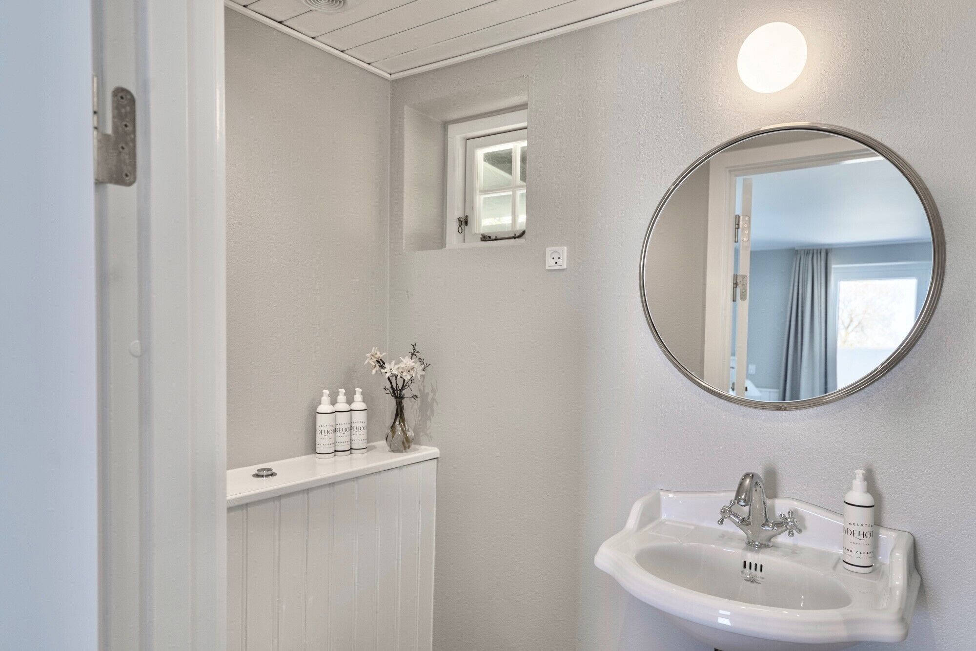 A bathroom with a white sink, a round mirror, and a small window above the mirror.