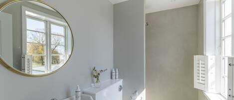 A bathroom with a white sink, mirror, and toilet. There is a window with white shutters and a view of trees outside.