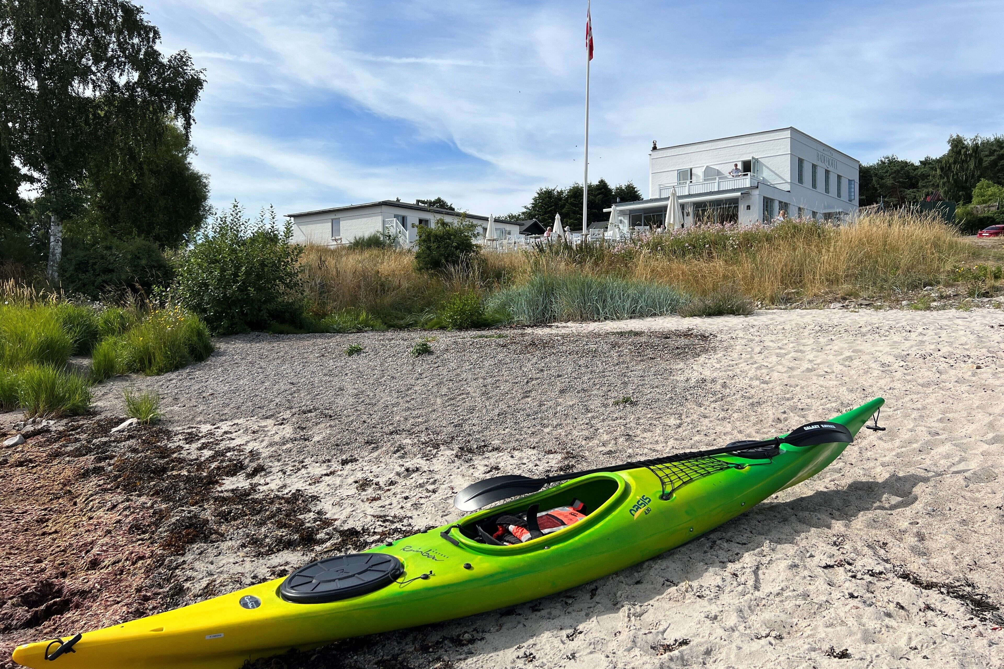 Un kayak verde sobre una playa arenosa, con un edificio al fondo.