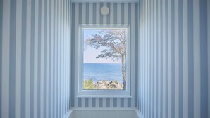 A room with a window framed in white, overlooking a tree and a body of water. - Melsted Badehotel  (Gudhjem)
