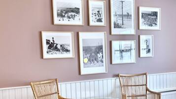 A wall with framed black and white photographs, two wicker chairs, and a glass table.