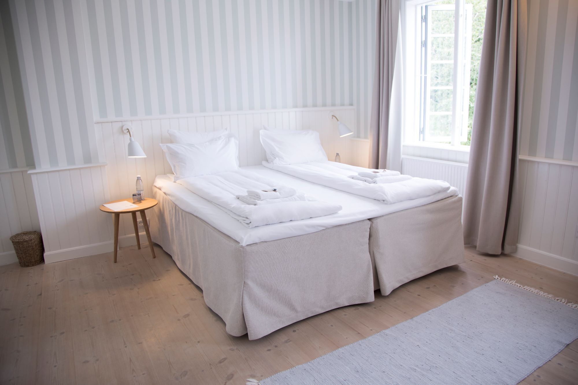 Un lit double avec du linge de lit blanc, une table de chevet avec une lampe et une fenêtre avec des rideaux.
