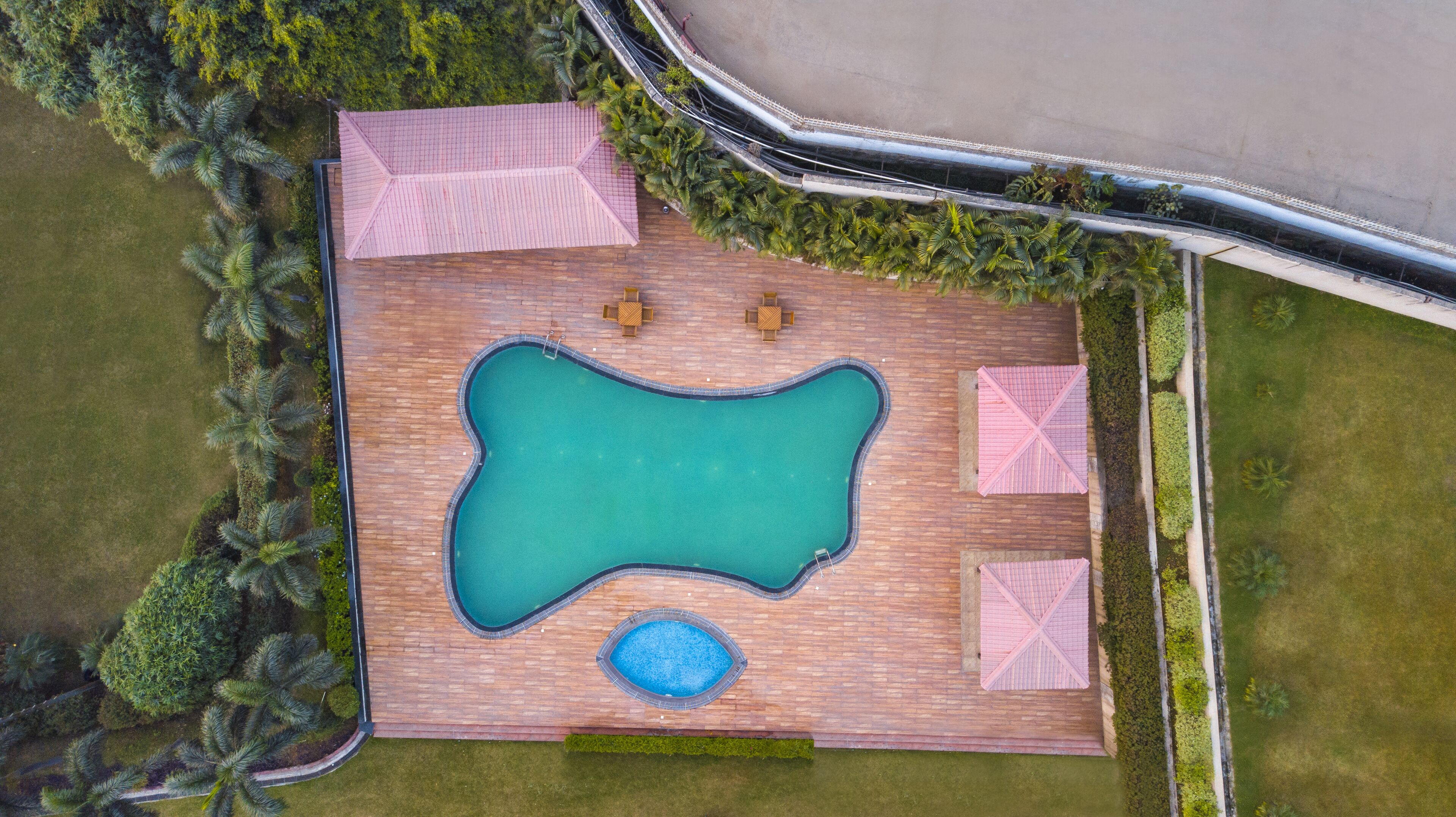 An aerial view of a swimming pool area with a wooden deck, two lounge chairs, and a small hot tub.