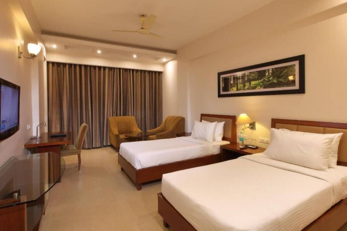 A hotel room with two beds, a desk with a TV, a chair, and a ceiling fan.