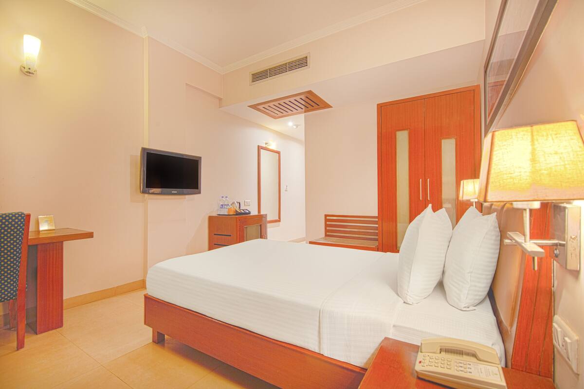 A hotel room with a bed, bedside table, lamp, TV, and a mirror.