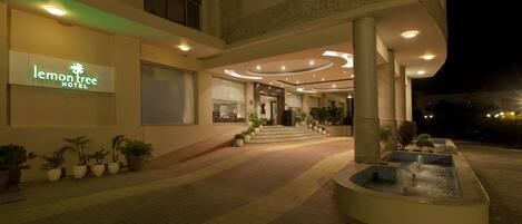 The exterior of the Lemon Tree Hotel with a well-lit entrance, a water feature, and potted plants.