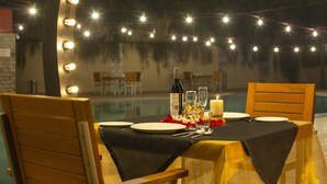 En uteservering med en pool, ljusslingor och ett bord dukat för två personer med tallrikar, bestick och ett ljus.
