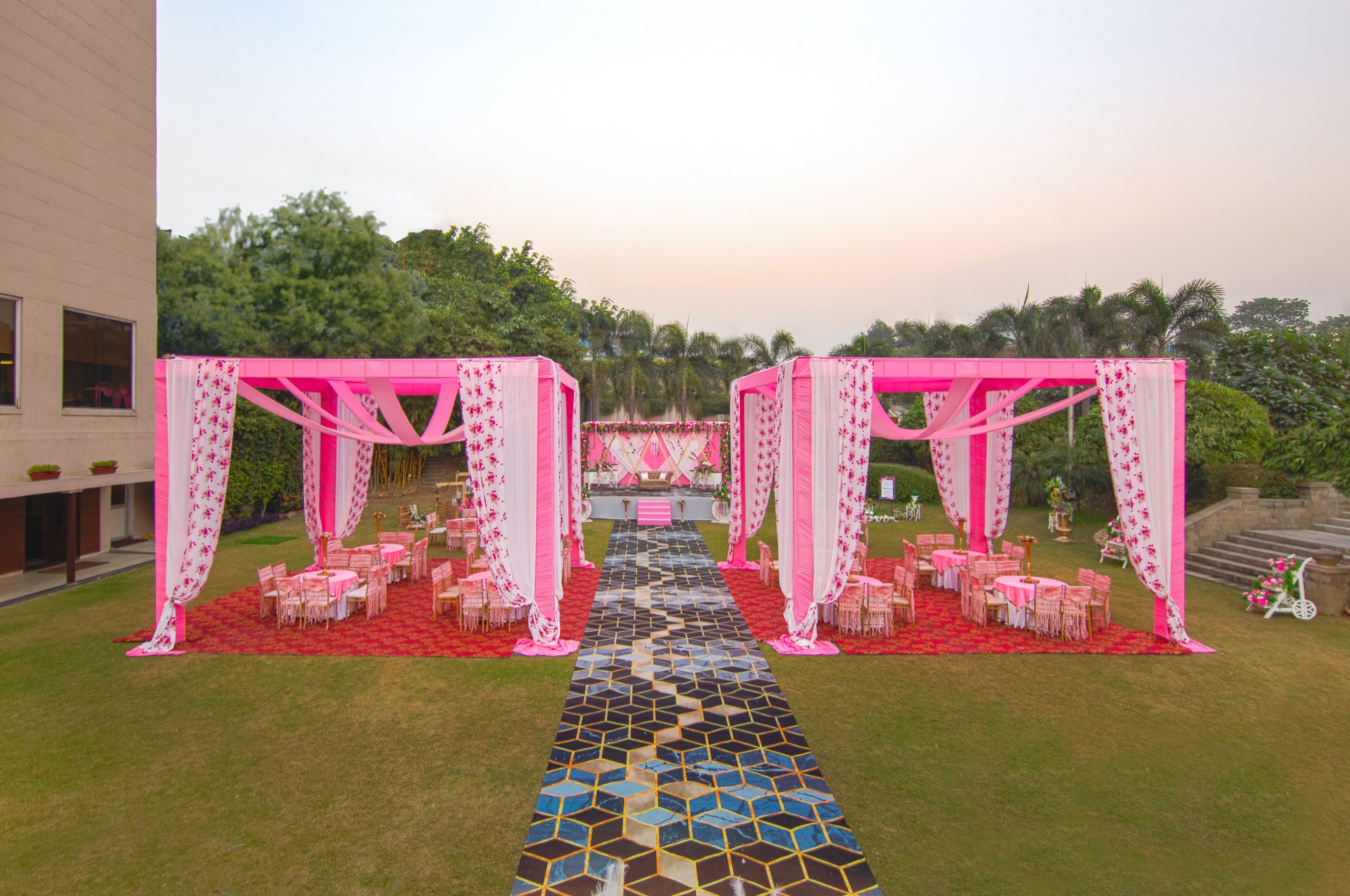 Decoración para boda al aire libre con un pasillo central que conduce a un escenario, rodeado de mesas y sillas.