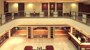 En hotellobby i flera nivåer med en central sittgrupp, glasräcken och en receptionsdisk.