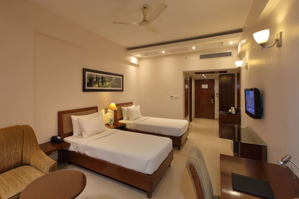 A hotel room with two beds, a sofa, a desk, a TV, and a ceiling fan.