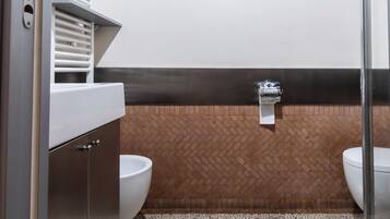 A modern bathroom with a herringbone tile floor, two toilets, a shower area, and a vanity with a towel rack.