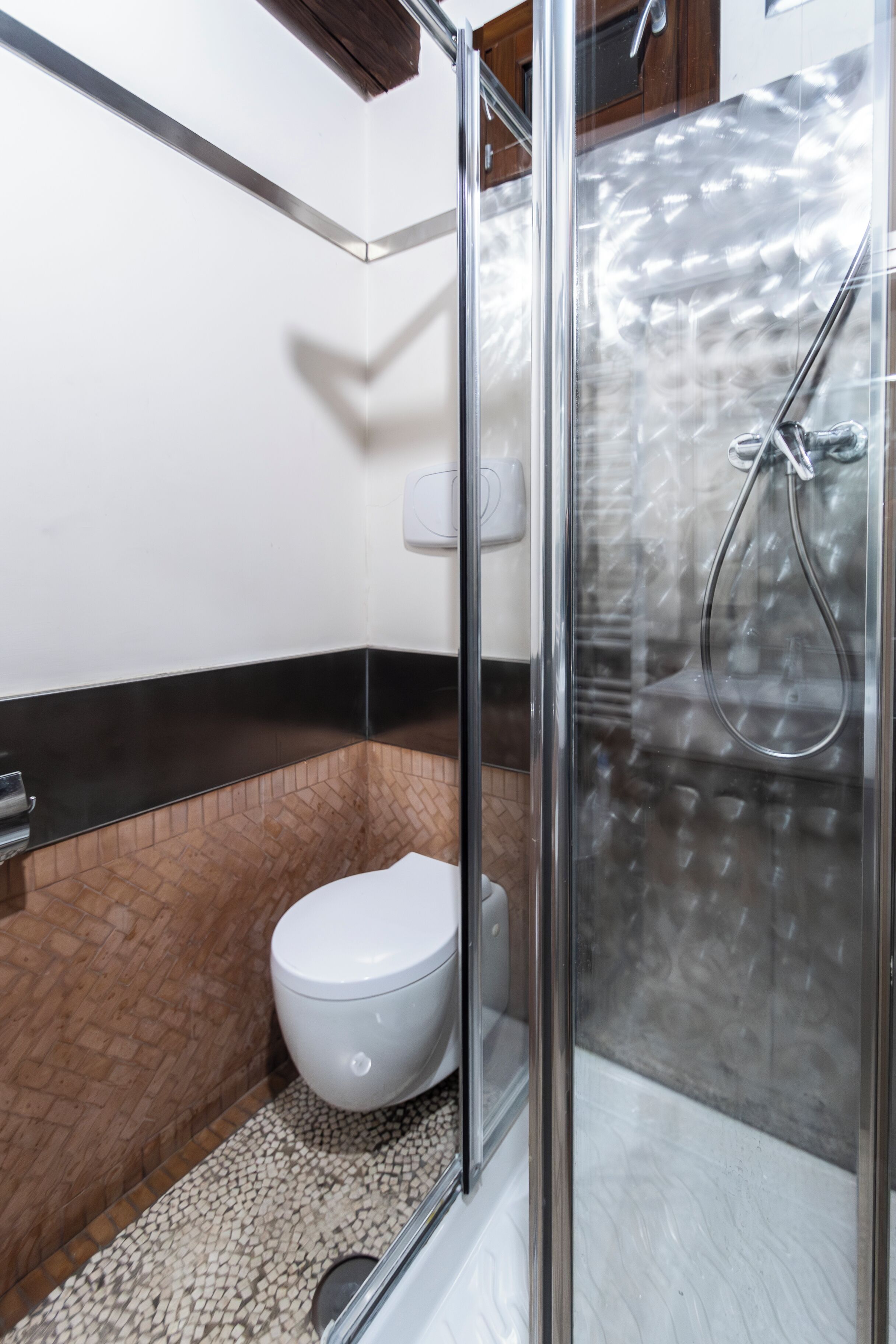 Une salle de bain moderne avec une douche à l’italienne en verre, des toilettes blanches et un sol carrelé de couleur marron.
