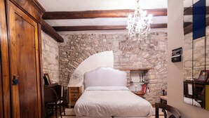 A bedroom with a stone wall, a wooden wardrobe, a bed, a desk, and a chandelier. - La Cantina del Convento (Potenza)