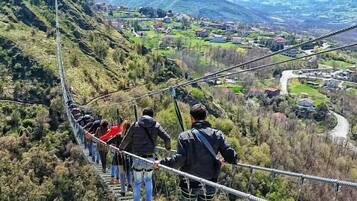 A group of people on a suspension bridge with a mountainous landscape in the background.