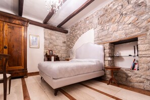 A bedroom with a stone wall, a bed, a wooden wardrobe, a small table, and a bookshelf. - La Cantina del Convento (Potenza)