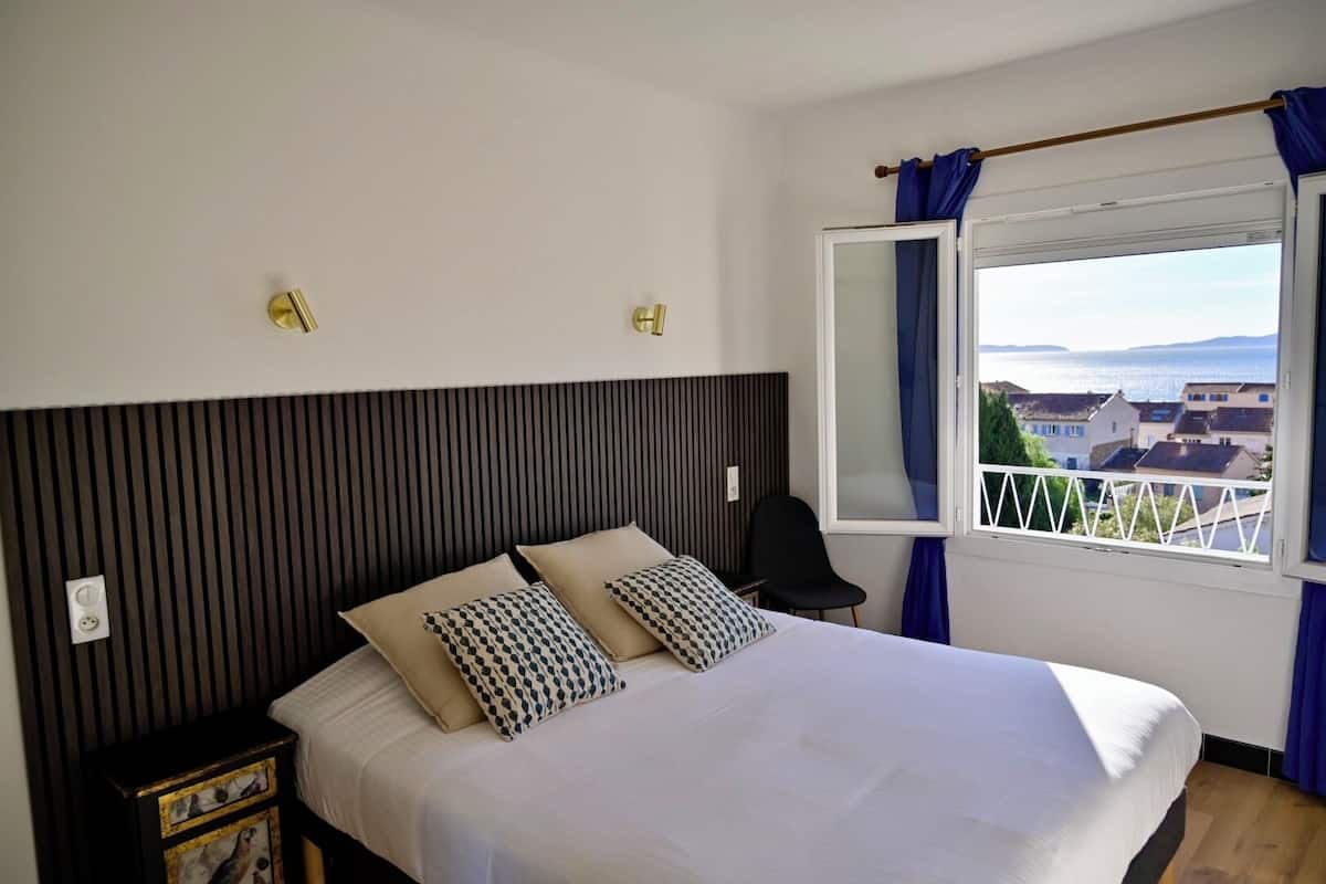 A bedroom with a bed, two bedside tables, a chair, a window with a view, and a curtain.