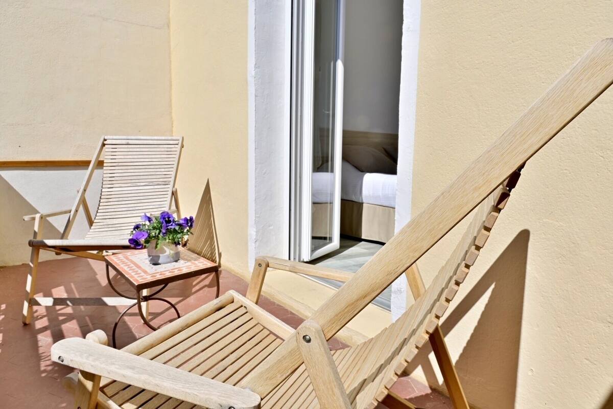 A balcony with wooden chairs and a small table with a vase of flowers.