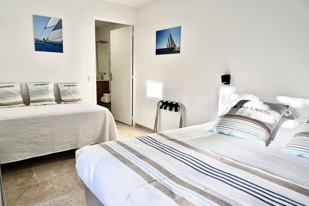 A hotel room with two beds, a shower area, and two sailboat pictures on the walls.