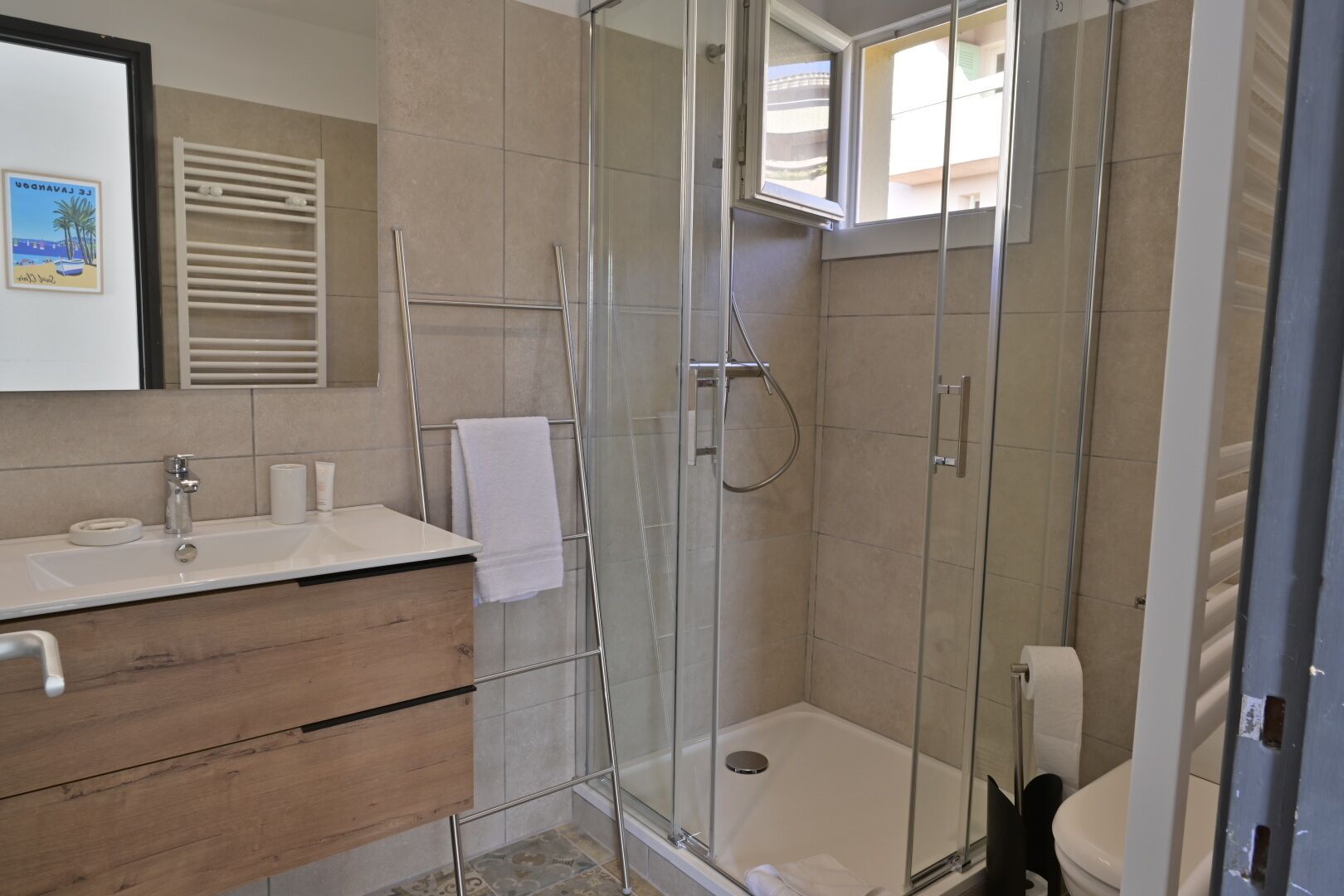 Un baño moderno con ducha envuelta en vidrio, tocador de madera, lavamanos blanco y retrete.