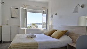 Habitación de hotel con cama, escritorio, silla, armario y ventana con cortinas, y vista al mar.