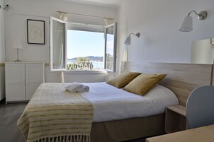 Habitación de hotel con cama, escritorio, silla, armario y ventana con cortinas, y vista al mar.