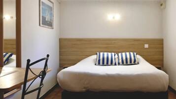 A single bed with a wooden headboard, a striped pillow, and a small bedside table.