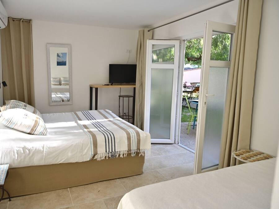 A bedroom with a bed, a desk, a TV, and a sliding glass door to a patio.