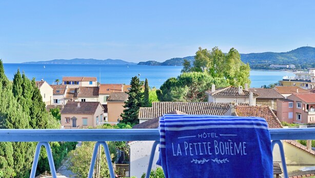 Vista desde un balcón con una toalla que dice "HOTEL LA PETITE BOHÊME" y un paisaje costero al fondo.