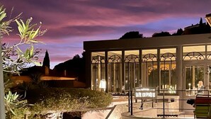 Un hotel con fachada de vidrio y ventanas en arco, rodeado de vegetación.
