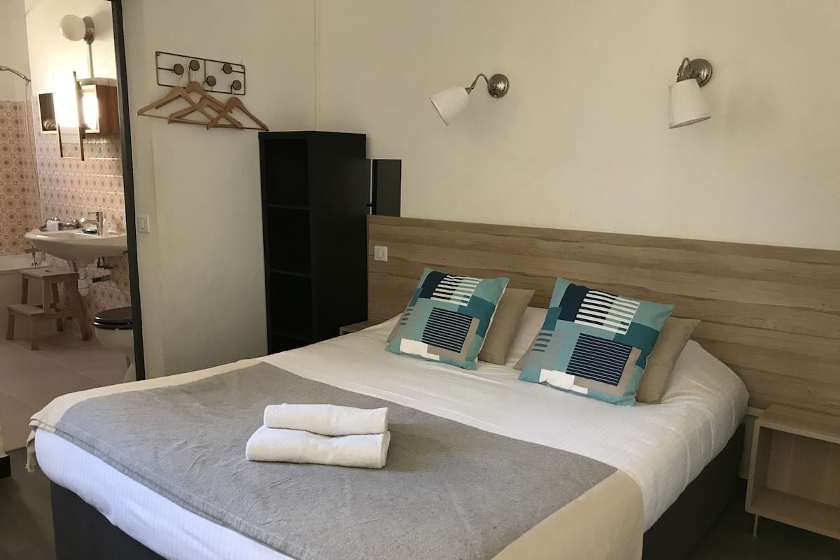 A neatly made bed with a grey blanket and two pillows, a bedside table with a lamp, and a wooden headboard.