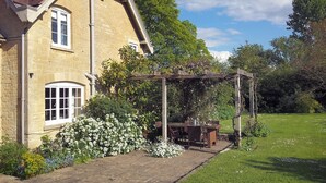 Ein Steinhaus mit Garten, einer Terrasse, einem Pergola und einem Rasen.