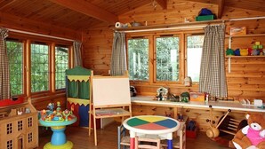 Ein gemütliches Holzhaus mit Spielbereich, darunter ein Tisch, Stühle und eine Spielküche.