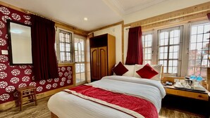 Habitación de hotel con una cama grande, suelo de madera, una mesita con una tetera y tazas, y vistas al exterior a través de amplios ventanales.