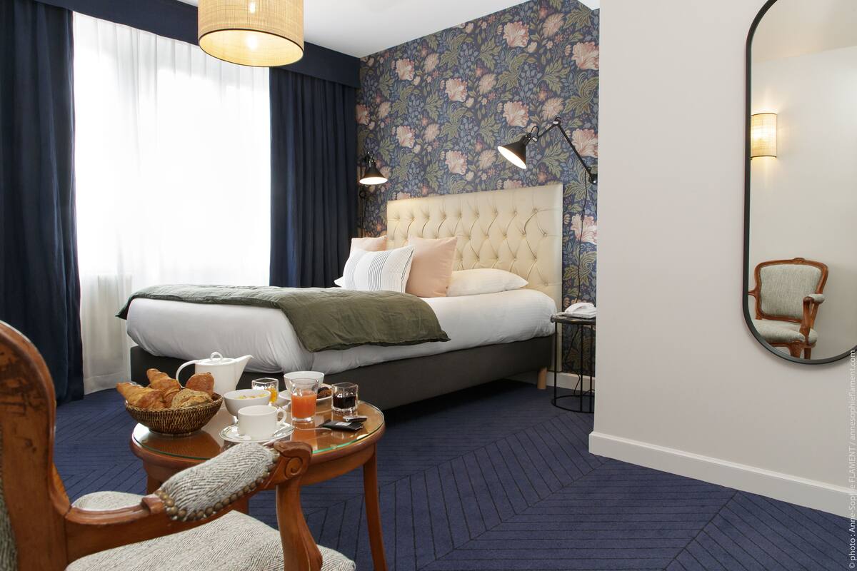 Ein Hotelzimmer mit Bett, Frühstückstisch mit Croissants, einer Kaffeemaschine und einem Glas Orangensaft.
